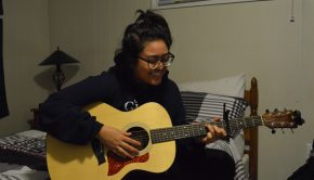 Young lady looks down while playing the guitar with a smile on her face.